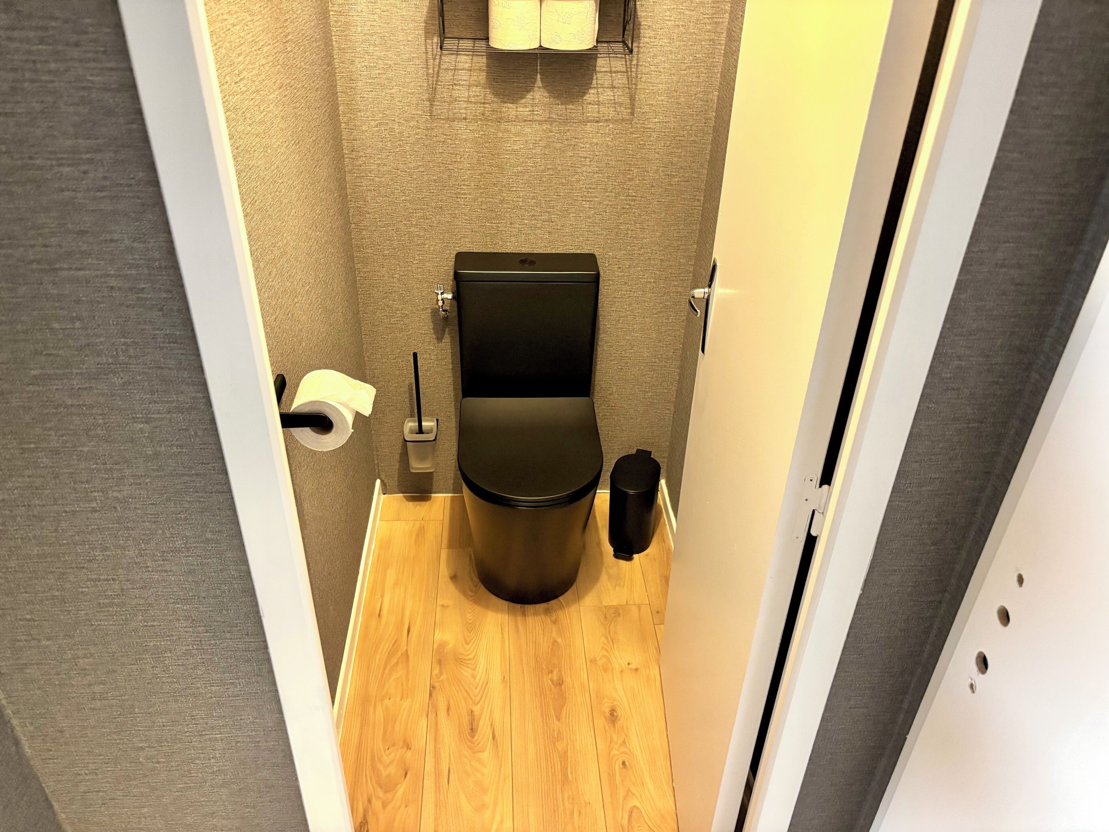 A compact bathroom with a toilet, a trash bin, and a toilet paper holder.