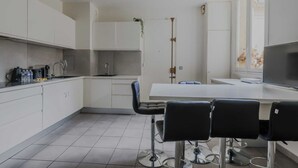 Een moderne keuken met witte kasten, een groot raam en een eethoek met barstoelen.