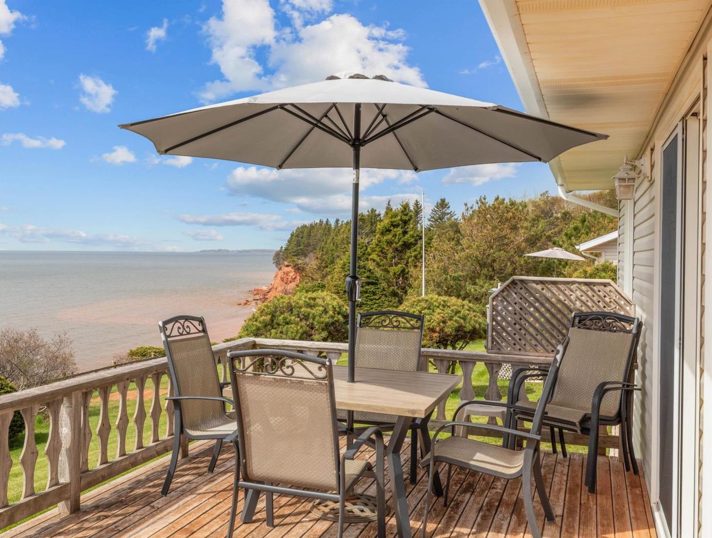 Une terrasse avec une table et des chaises, un parasol et une vue sur l’océan.