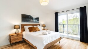 Une chambre moderne avec un lit en bois, deux tables de chevet avec des lampes, une grande fenêtre avec des rideaux et un tableau au-dessus du lit.