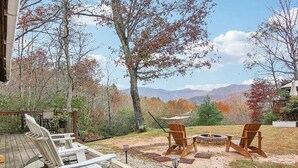 A deck with Adirondack chairs, a fire pit, and a view of mountains.