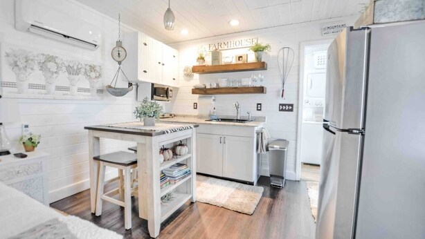 A modern kitchen with white cabinetry, a wooden island, a stainless steel refrigerator, and a farmhouse sign on the wall.