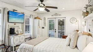 A bedroom with a bed, a coffee bar, a television, and a ceiling fan.