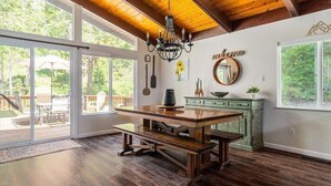 Un comedor amplio con una mesa de madera y bancos, una araña y vistas a un patio exterior a través de puertas correderas de vidrio.