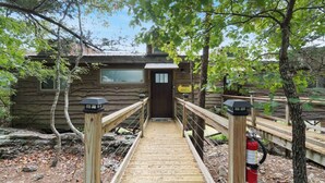 A wooden bridge leading to a rustic cabin with a wooden door and a sign indicating "Sunset 44". - Modern Retreat, King Suite, River Views (Carroll County)