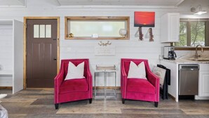 A room with two red velvet chairs, a wooden door, a window with a view, a kitchen area with a sink and dishwasher, and a wall-mounted artwork. - Modern Retreat, King Suite, River Views (Carroll County)