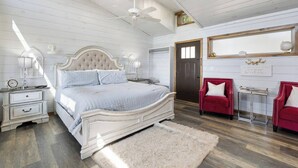 A bedroom with a large bed, two nightstands, a red chair, a mirror, and a ceiling fan. - Modern Retreat, King Suite, River Views (Carroll County)