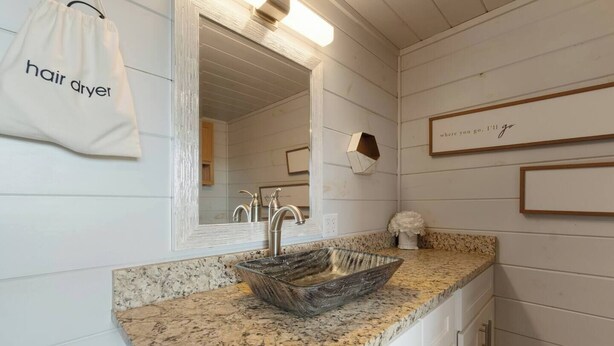 A bathroom with a granite countertop, a glass bowl sink, a mirror, a hair dryer bag, and a framed quote on the wall. - Modern Retreat, King Suite, River Views (Carroll County)
