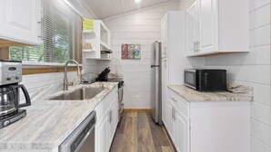 A compact kitchen with white cabinets, a built-in dishwasher, a coffee maker, and a microwave. - Modern Retreat, King Suite, River Views (Carroll County)