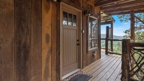 Una cabaña de madera con un amplio portal, un felpudo y vistas del paisaje circundante.