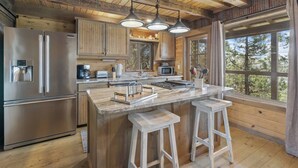 Una cocina moderna con refrigerador de acero inoxidable, gabinetes de madera, encimera de mármol y un ventanal con vistas a árboles.