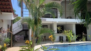 A modern building with a pool, surrounded by various plants and a clear blue sky. - Beautiful complex with swimming pool, close to the beach and downtown. (Sámara)