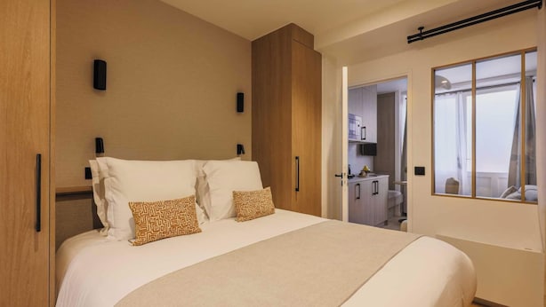 Habitación de hotel moderna con una cama grande, armario de madera y vistas por la ventana.