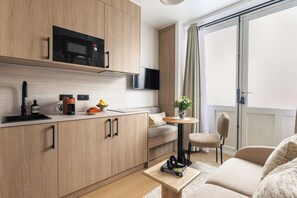 A modern kitchen with a microwave, coffee machine, and a flat-screen TV. There is a dining area with a table and chairs, and a sofa in the living room. - Elegant Apartment - 1br- 4P- Trocadero (Paris)