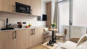 Una cocina moderna con microondas, cafetera y televisor de pantalla plana. Hay un comedor con mesa y sillas, y un sofá en la sala.