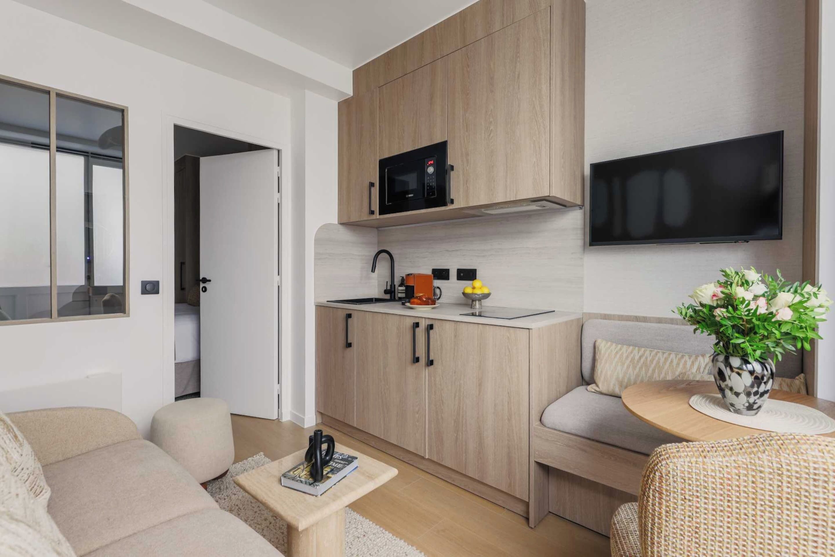 Un espace de vie moderne comprenant un coin cuisine, un canapé, une petite table et un téléviseur fixé au mur.