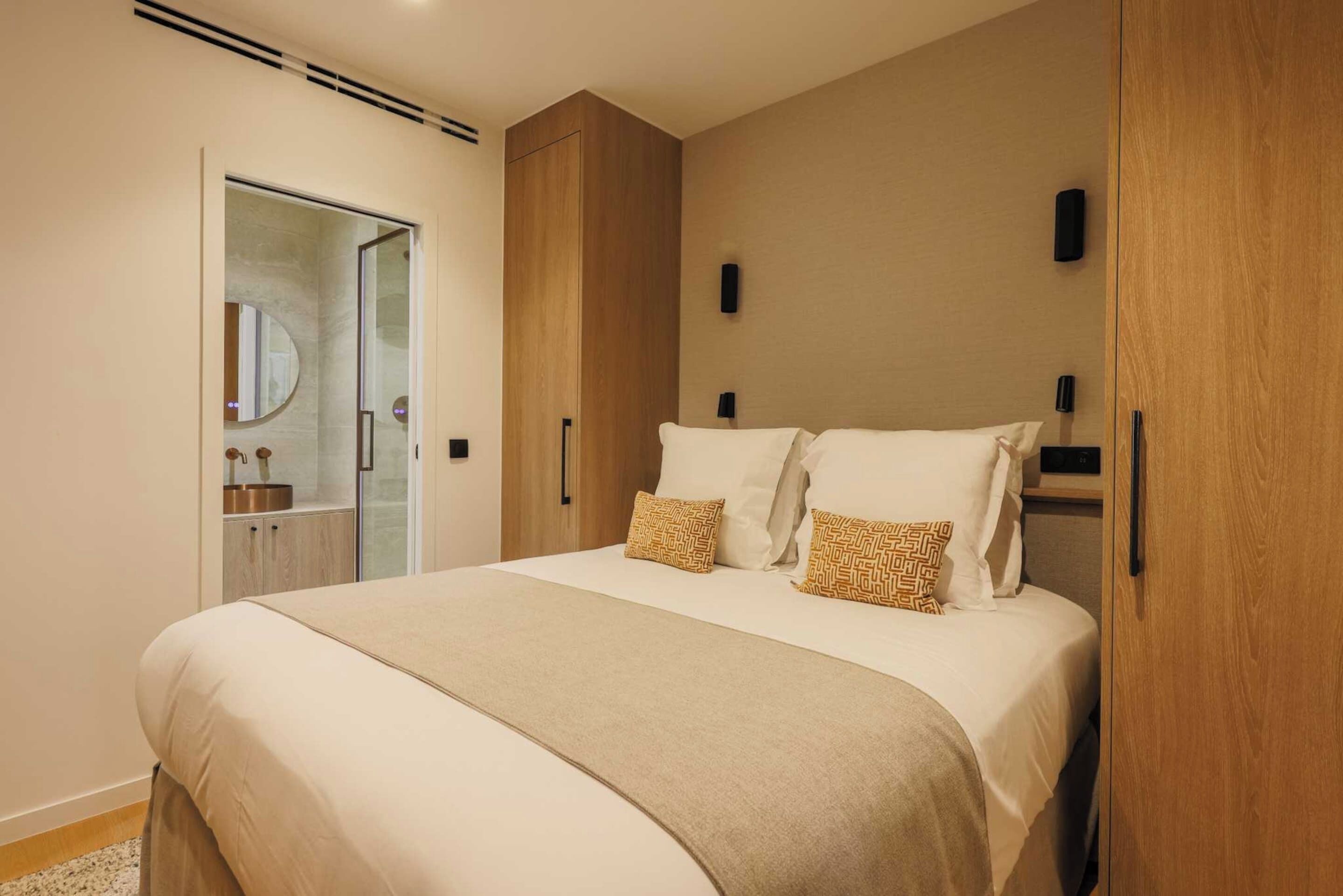A bedroom with a bed, bedside tables, a wardrobe, and a bathroom with a mirror and sink.