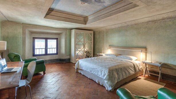 Un dormitorio con una cama grande, un escritorio con una computadora portátil, sillas verdes, una ventana y un techo decorativo.