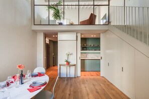 Un comedor moderno con suelo de madera, una mesa para cuatro comensales y una cocina al fondo.