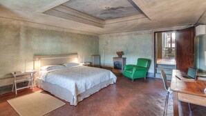 Un dormitorio con una cama grande, un escritorio con una computadora portátil, una silla verde y una chimenea.
