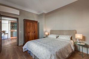 Un dormitorio con una cama grande, dos mesitas de noche con lámparas, un armario de madera y una puerta que da a la cocina.