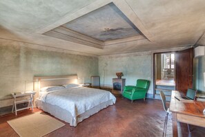 A bedroom with a large bed, a desk with a laptop, a green chair, and a fireplace.