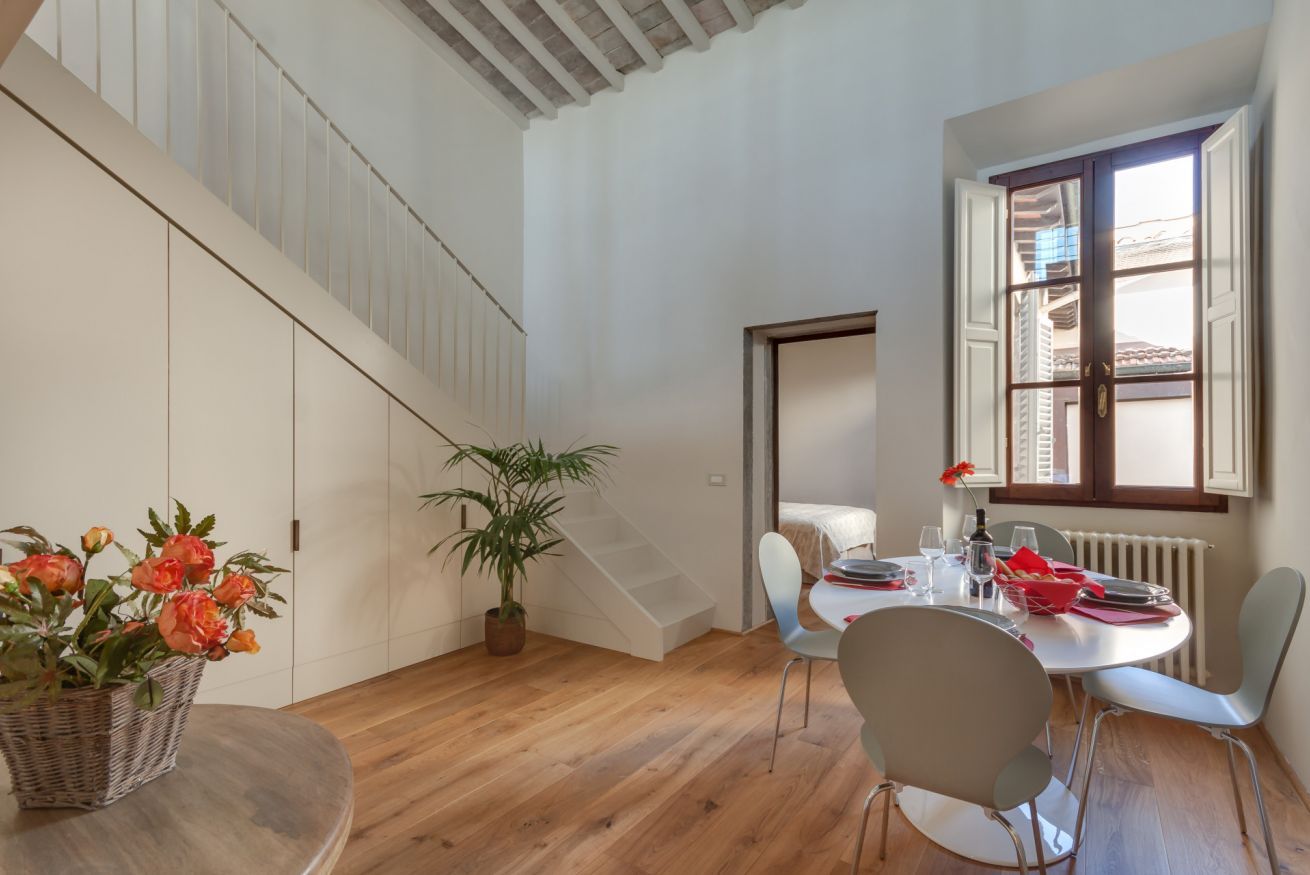 A dining area with a round table, chairs, a potted plant, and a staircase.