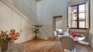 Un comedor con una mesa redonda, sillas, una planta en maceta y una escalera.