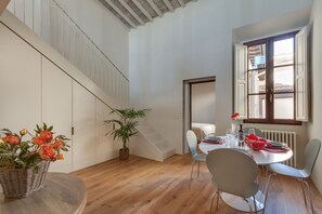 A dining area with a round table, chairs, a potted plant, and a staircase.