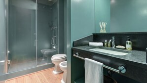 Un baño moderno con cabina de ducha de vidrio, inodoro blanco y encimera negra con lavamanos y artículos de aseo.