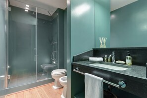 A modern bathroom with a glass shower enclosure, a white toilet, and a black countertop with a sink and toiletries.