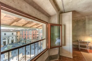 A room with a large window overlooking a courtyard with buildings. There is a white door and a small table with a lamp. - Accademia Frescoes Apartment (Firenze)