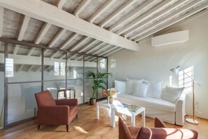 A modern living room with a wooden floor, a white sofa, a red armchair, a coffee table, and a floor lamp. - Accademia Frescoes Apartment (Firenze)