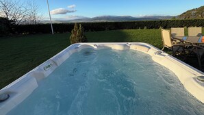 Un jacuzzi en un patio trasero con vistas a montañas y un seto.