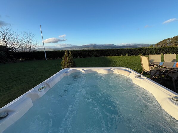 A hot tub in a backyard with a view of mountains and a hedge.