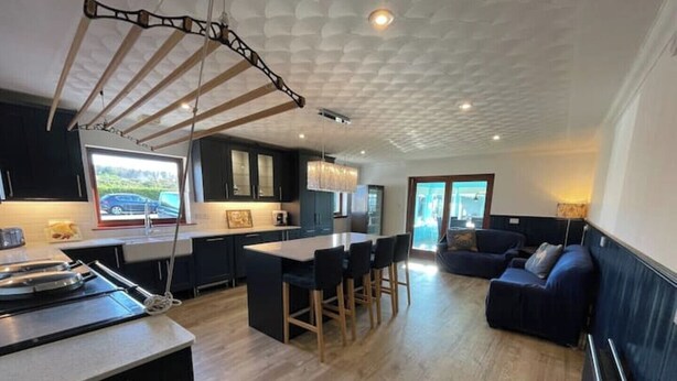Una cocina moderna con armarios oscuros, una mesa de comedor de madera y una lámpara colgante.