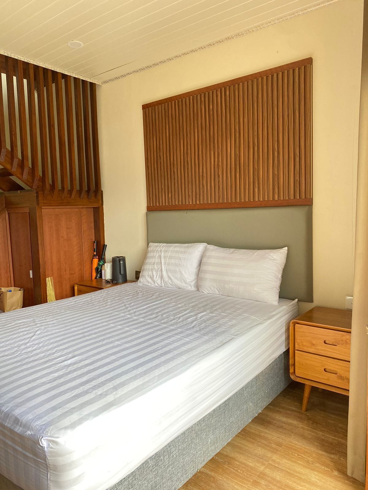 A neatly made bed with a striped bedspread, a wooden headboard, and a wooden nightstand with drawers.