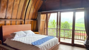 A wooden-framed room with a bed, a small table, and a balcony with a view of greenery. - Villa Anteng (Sidemen)