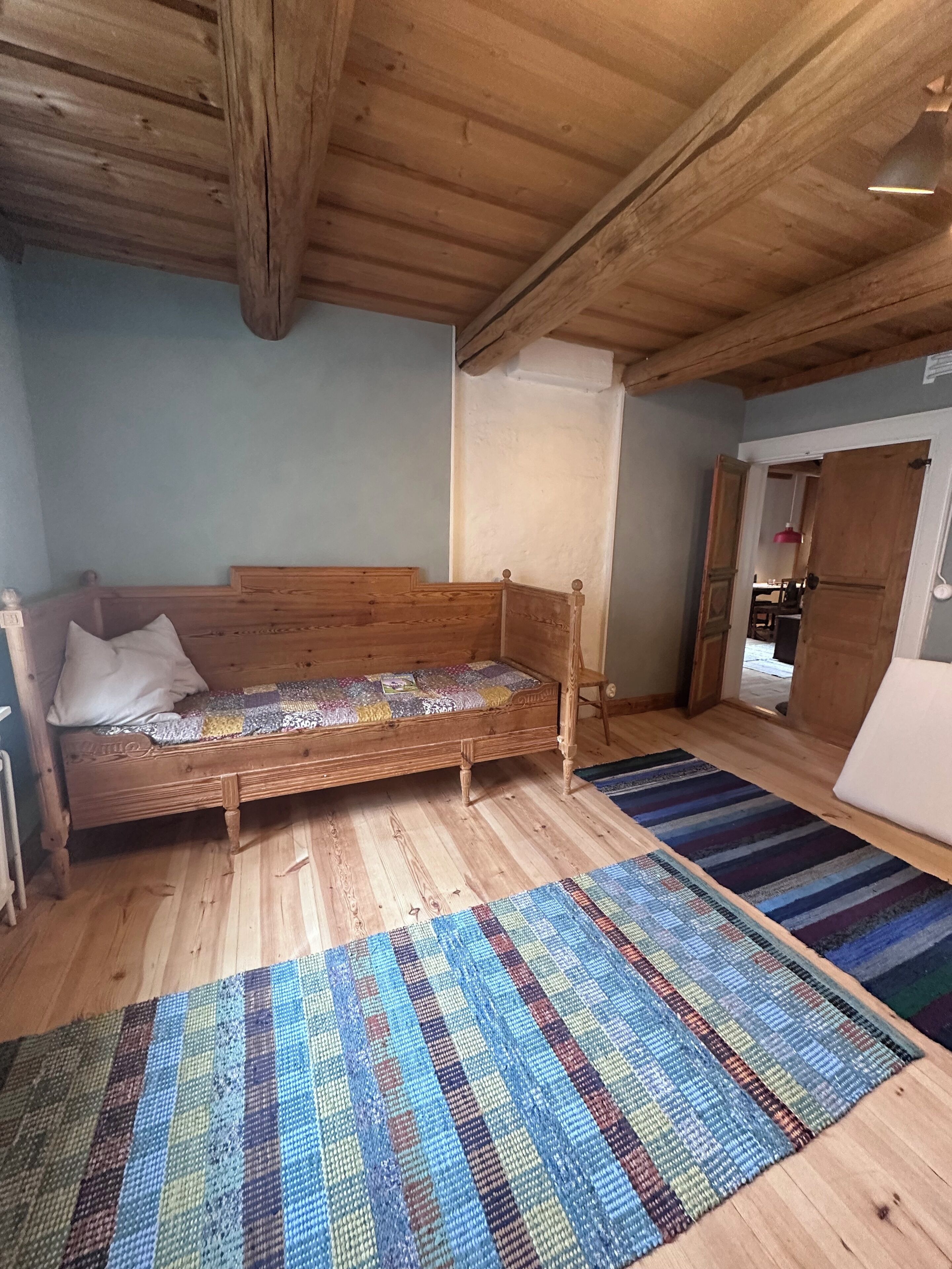 Una cama de madera con colcha, un tapete azul y de varios colores, y un techo de madera.