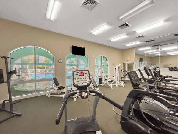 A gym with treadmills, exercise machines, and large windows overlooking a swimming pool. - Unit 1002 - An updated relaxing 2BR/2BA condo w/private bunk room in Panama City (Panama City)