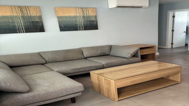 Un salon moderne avec un canapé d’angle, une table basse en bois et deux tableaux abstraits accrochés au mur.