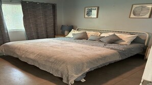 Une chambre avec un grand lit, une table de chevet avec une lampe et deux tableaux encadrés accrochés au mur.