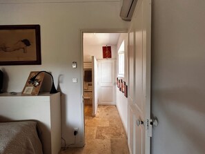 Een gang met een deur die naar een kamer leidt, een kapstok, een stopcontact en een lijst aan de muur.