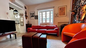 A living room with a red sofa, a television, and a large window. - Villa Hyacinthe (Saint-Étienne-du-Grès)