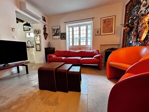 Ein Wohnzimmer mit einem roten Sofa, einem Fernseher und einem großen Fenster.