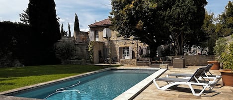 Una piscina con muelle de madera, sillas de descanso y patio de piedra.