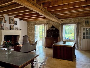 Een rustiek interieur met een stenen muur, houten balken, een open haard en een eethoek.