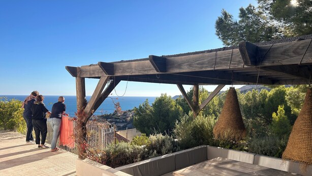 Een terras buiten met een houten pergola, een zithoek en uitzicht op zee.