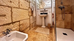 A bathroom with a stone wall, a sink, a mirror, and a shower. - Villa Hyacinthe (Saint-Étienne-du-Grès)