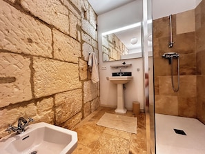 Ein Badezimmer mit Steinwand, Waschbecken, Spiegel und Dusche.